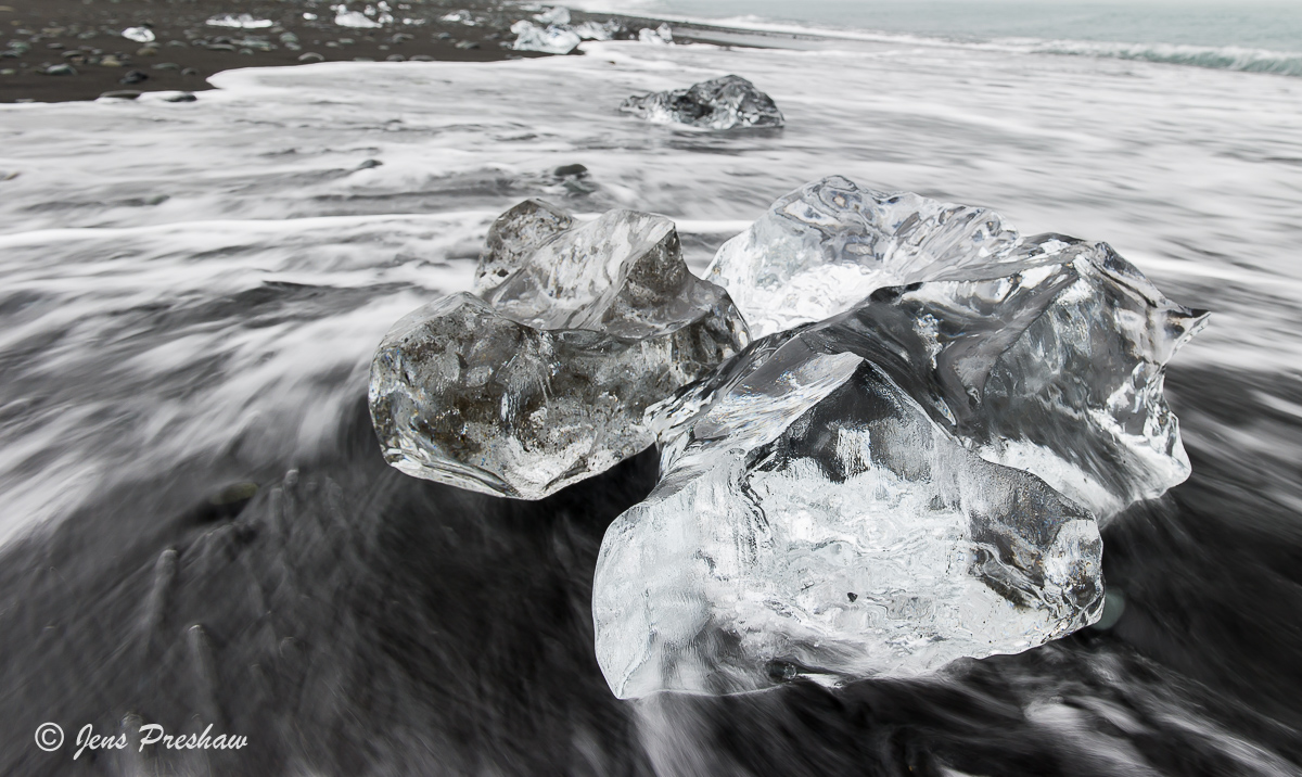 Chunks of glacial ice are washed up on a beach with black volcanic sand by the North Atlantic ocean.